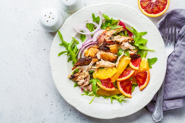 Pollo alla griglia e insalata di arancia con cipolla in zolla bianca su sfondo bianco.