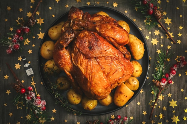 Pollo caldo con patate in un piatto e una corona di rami di abete su un tavolo di legno nero