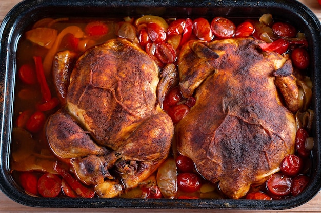 Pollo croccante dorato intero al forno cotto in salsa primo piano in una teglia sul tavolo di legno