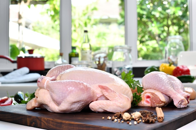 Pollo crudo fresco con ingredienti per cucinare su un tagliere di legno in cucina