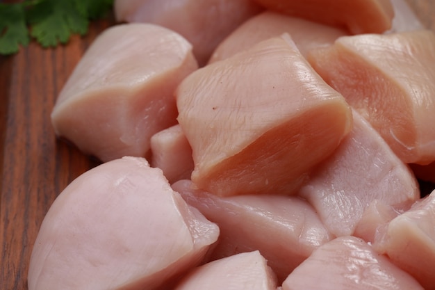 Pollo crudo tenero fritto tagliato senza pelle disposto su tavola di legno e guarnito con foglie di coriandolo