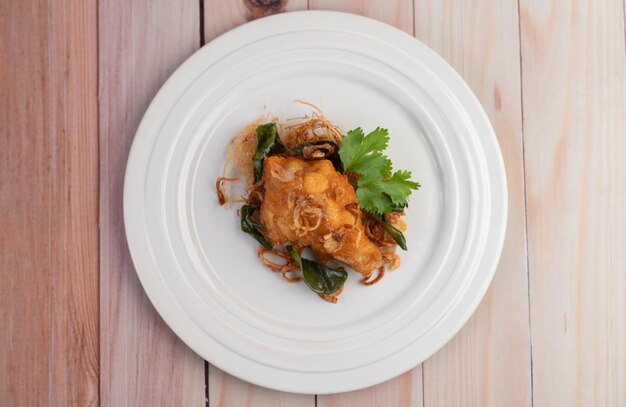 Pollo fritto con erbe su un piatto bianco su un pavimento di legno