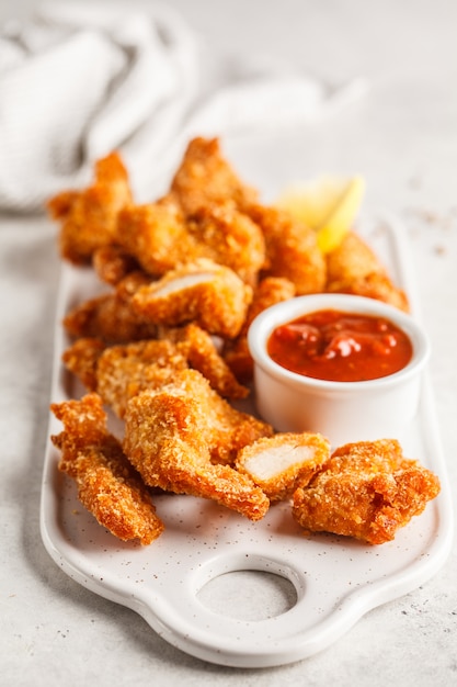 Pollo impanato fritto con salsa al pomodoro su un bordo bianco.