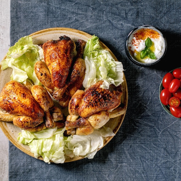 Pollo intero arrosto con insalata verde su piatto di ceramica salsa di yogurt pomodorini su tovaglia di lino blu Immagine quadrata piatta