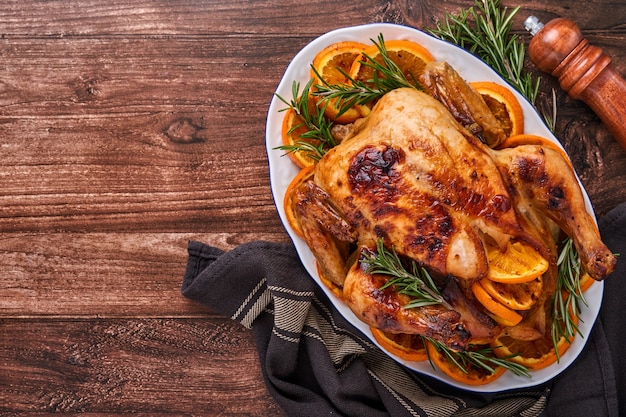 Pollo intero arrosto o al forno con rosmarino e arance, fatto in casa per una cena in famiglia su un tavolo di pietra marrone. Vista dall'alto con copia spazio.