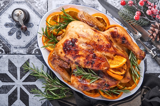 Pollo intero arrosto o al forno con rosmarino e arance, fatto in casa per una cena in famiglia su un tavolo di pietra marrone. Vista dall'alto con spazio di copia.