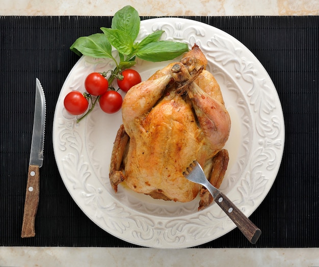 Pollo intero arrosto su un piatto con pomodori e basilico