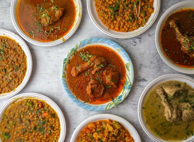 Pollo o manzo rosso karahi daal moong mash chana channay korma nihari fry makhni qeemawhite karahi servito in un piatto isolato sul tavolo vista dall'alto del cibo indiano e pakistani desi assortiti