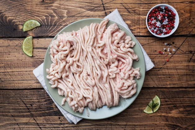 Pollo tritato crudo su un piatto con spezie e lime.