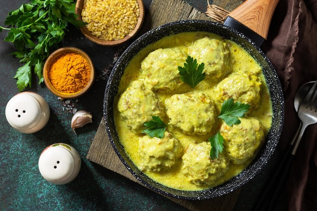 Polpette con bulgur in panna acida e salsa di curcuma in padella su un piano di lavoro in pietra scura Vista dall'alto