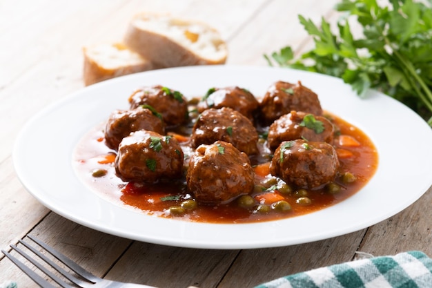 Polpette di carne, piselli verdi e carote con salsa di pomodoro su un tavolo di legno.