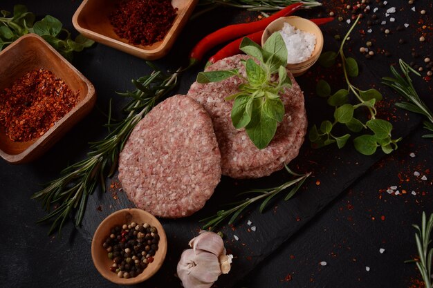 Polpette di hamburger di manzo crudo con erbe e spezie. Cotolette di hamburger crude su uno sfondo di cemento