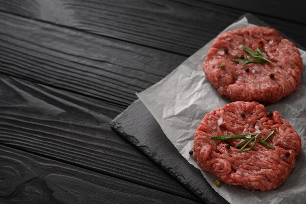 Polpette di hamburger di manzo crudo su tavola di legno del macellaio rosmarino e pepe Sfondo nero Vista dall'alto