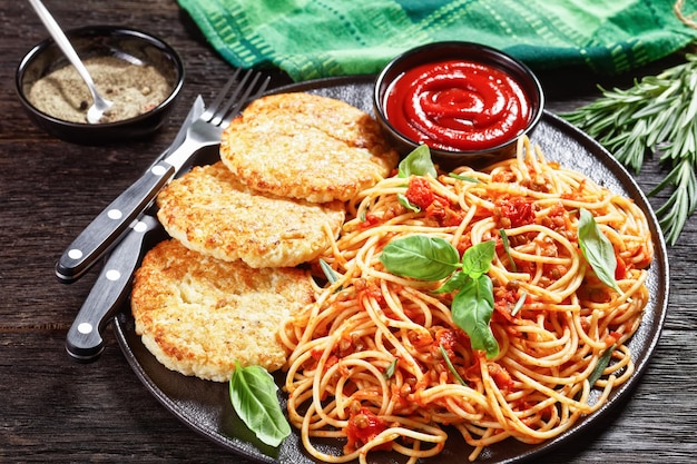 Polpette di merluzzo servite su un piatto nero con spaghetti misti di lenticchie, salsa di pomodoro ed erbe aromatiche, vista orizzontale dall'alto