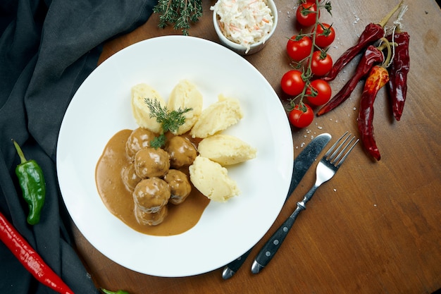 Polpette di pollo appetitose in salsa con un contorno di purè di patate in un piatto bianco su un tavolo di legno in una composizione con ingredienti