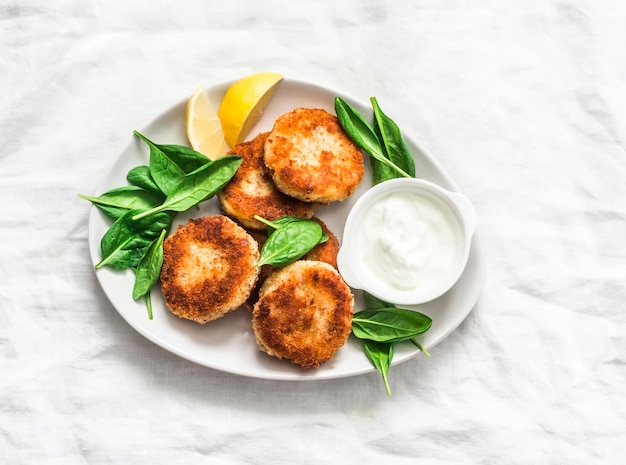 Polpette di tonno e patate servite con spinaci e yogurt greco su sfondo chiaro vista dall'alto