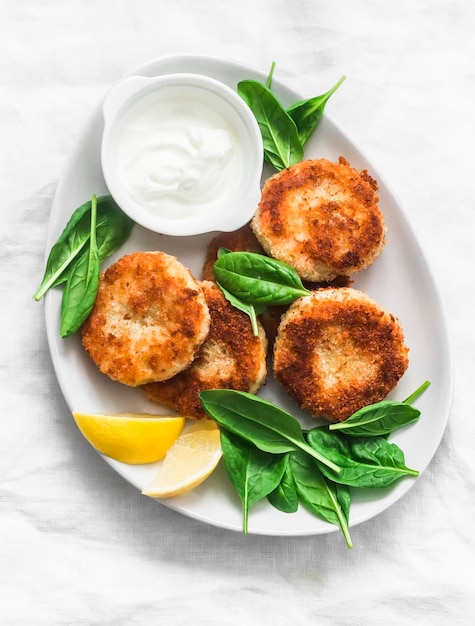 Polpette di tonno e patate servite con spinaci e yogurt greco su sfondo chiaro vista dall'alto