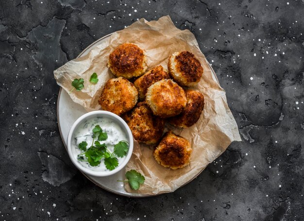 Polpette di tonno in scatola di patate con salsa di coriandolo allo yogurt greco su sfondo scuro vista dall'alto