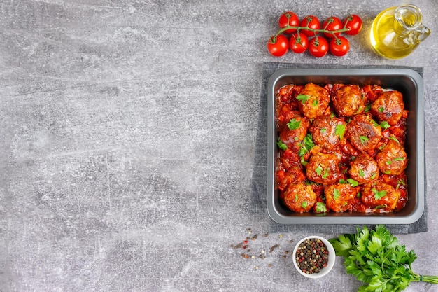 Polpette fatte in casa con salsa di pomodoro e spezie servite in padella nera su sfondo grigio cemento