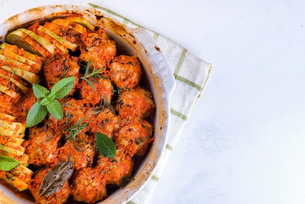 Polpette fatte in casa con salsa di pomodoro in un piatto bianco cotte al forno con erbe su marmo bianco