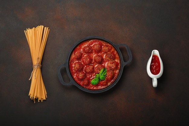 Polpette in salsa di pomodoro con spezie e basilico in una padella con pasta e salsa-boaton arrugginito sfondo marrone