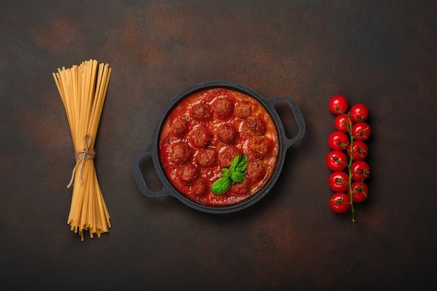 Polpette in salsa di pomodoro con spezie, pomodorini, pasta e basilico in una padella su sfondo marrone arrugginito