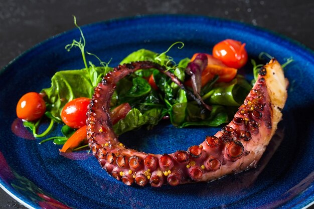 Polpo fritto con pomodori ed erbe aromatiche su un piatto blu