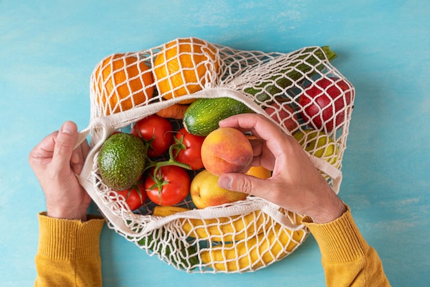 Polso dell'uomo che prende il frutto della pesca dalla borsa della spesa in rete con frutta e verdura Shopping ecologico Stile di vita sostenibile