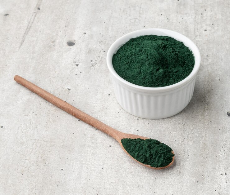 Polvere di alga Spirulina in una ciotola e cucchiaio sopra il tavolo di legno.