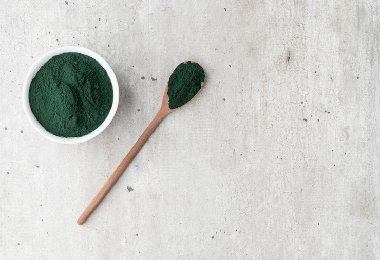 Polvere di alghe spirulina in una ciotola e cucchiaio su un tavolo di legno con spazio per le copie.