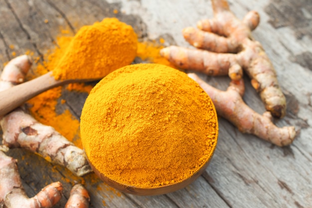 Polvere di curcuma e curcuma fresca in ciotola di legno sul tavolo di legno. Erbe aromatiche