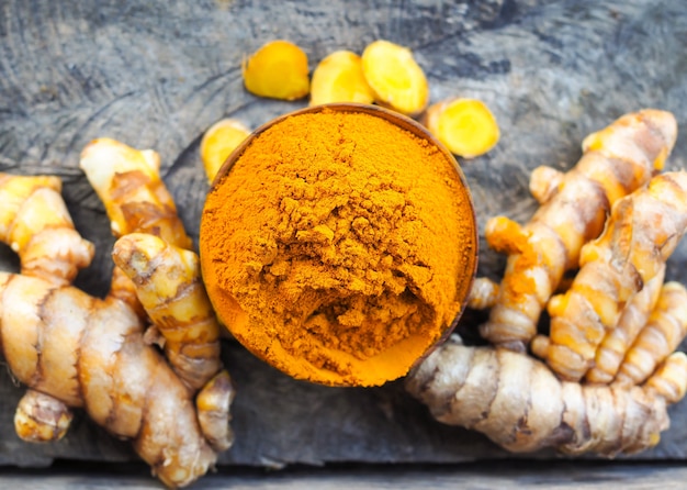 Polvere di curcuma e curcuma fresca in ciotole di legno sul vecchio tavolo di legno