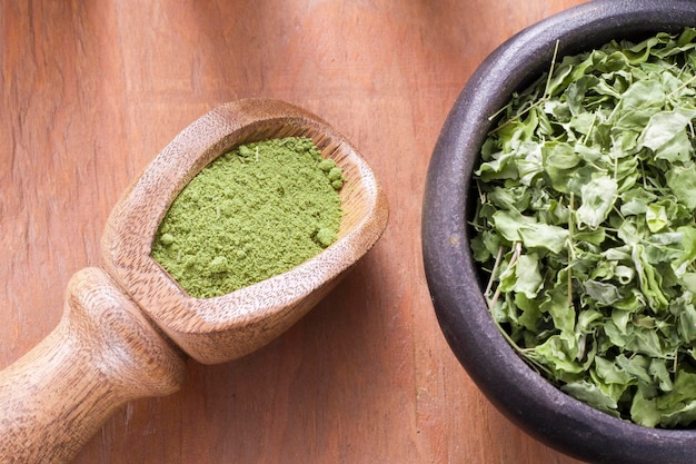 Polvere e foglie di moringa in una ciotola su fondo di legno