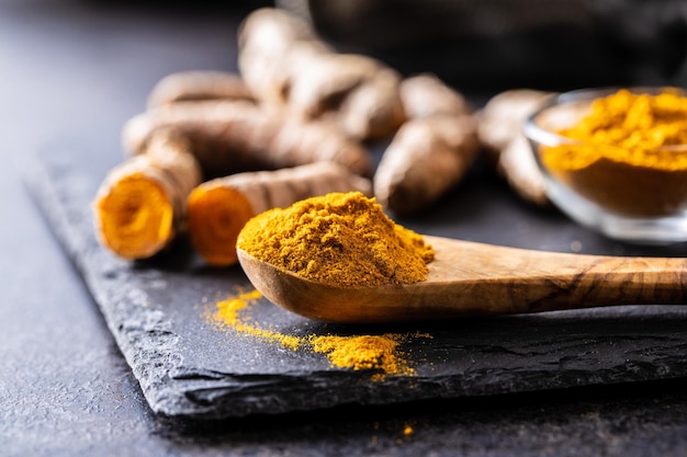 Polvere e radice di curcuma indiana Spezie di curcuma Curcuma macinata in un cucchiaio di legno