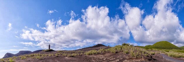 Polvere vulcanica e strada sullo sfondo del cielo azzurro delle montagne con nuvole e faro nelle Azzorre