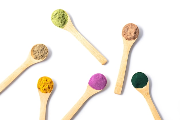 Polveri superfood multicolori in cucchiai di legno patata dolce matcha spirulina canapa curcuma carruba su sfondo bianco Orientamento orizzontale vista dall'alto