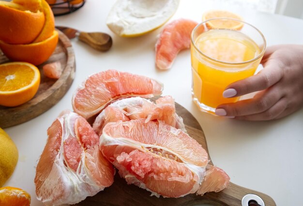 Pomelo in un taglio su un supporto di legno vicino a un bicchiere di succo appena spremuto e arance