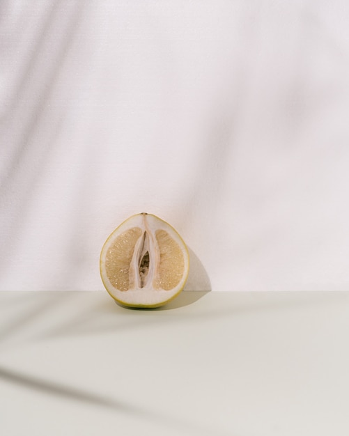 Pomelo su sfondo bianco e verde pastello. Ombre morbide di foglie di palma. Arte concettuale di cibo minimale estivo o primaverile.