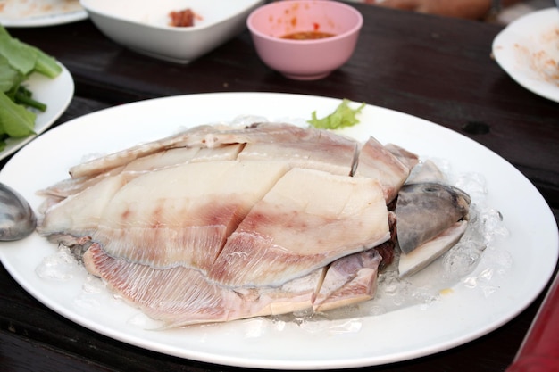 Pomfret grigio fresco Pesce pomfret d'argento cinese tagliato a pezzi disposti in un piatto bianco condito con ghiaccio Sul tavolo di legno nel ristorante prepararsi per lo shabu pot Messa a fuoco selettiva