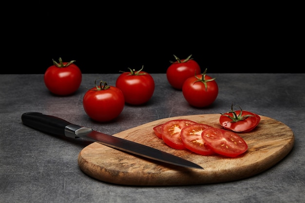 Pomodori affettati su un tagliere di legno marrone con un coltello su uno sfondo scuro. Vista laterale