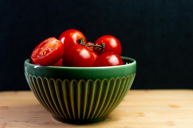 Pomodori all'interno di una ciotola verde su un tavolo di legno con sfondo nero