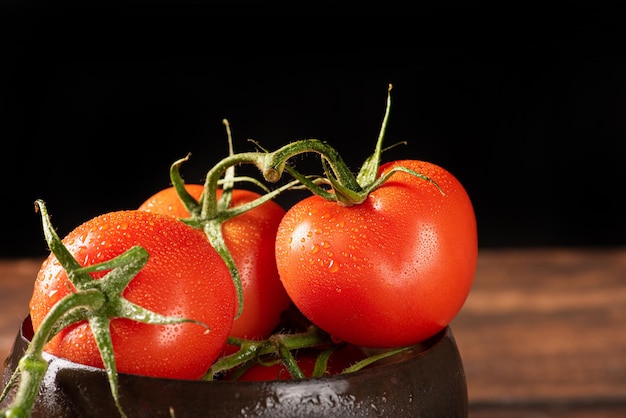 Pomodori bellissimi pomodori posti in una pentola di legno su un tavolo rustico sfondo nero fuoco selettivo