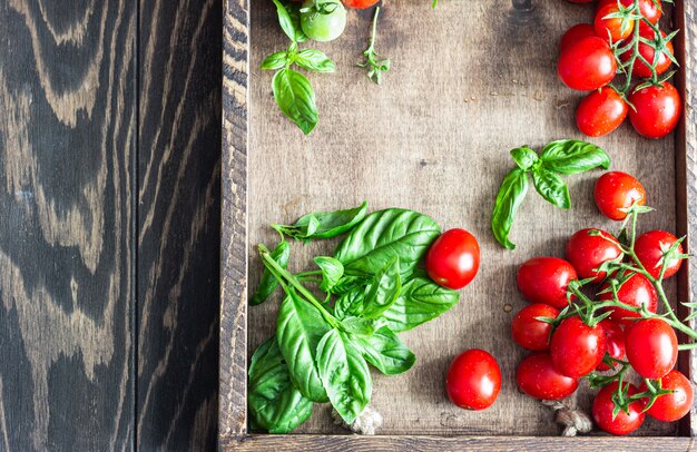 Pomodori ciliegia e basilico maturi freschi su una superficie di legno.