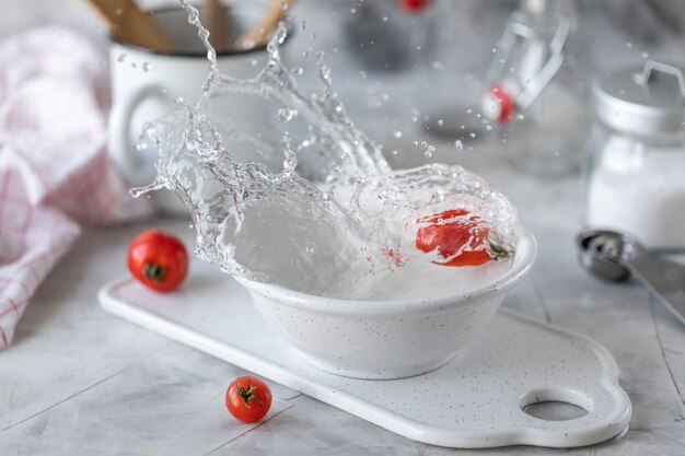 Pomodori ciliegia e foglie rossi freschi del basilico in un piatto su un tavolo da cucina bianco.