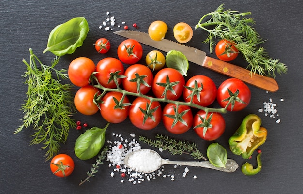 Pomodori ciliegia, erbe aromatiche e sale su una vista dall'alto del bordo scuro