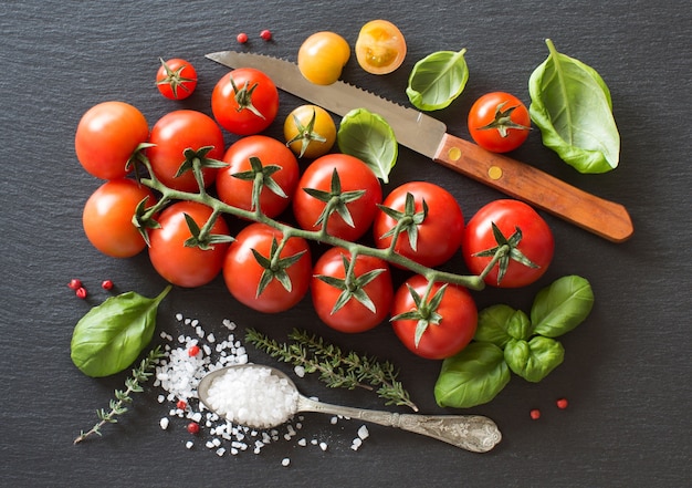 Pomodori ciliegia, erbe aromatiche e sale su una vista dall'alto del bordo scuro