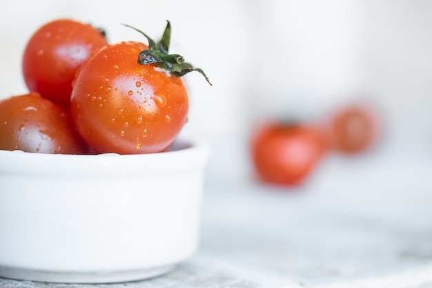 Pomodori ciliegia in ciotola ceramica bianca su legno bianco