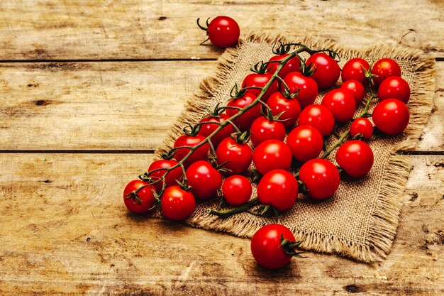 Pomodori ciliegia maturi interi sul ramo. Nuovo raccolto, su tela di sacco, fondo dei bordi di legno, spazio della copia