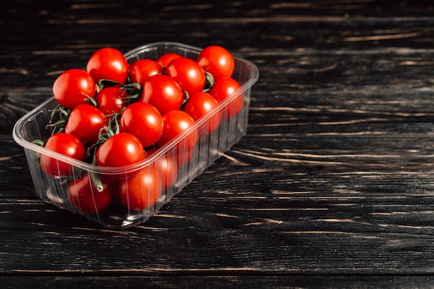 Pomodori ciliegia nella scatola di plastica sulla tavola di legno