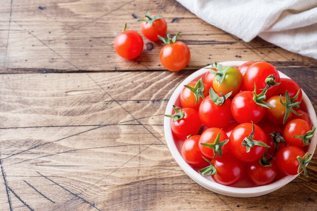 Pomodori ciliegia rossi in ciotola ceramica sulla tavola di legno